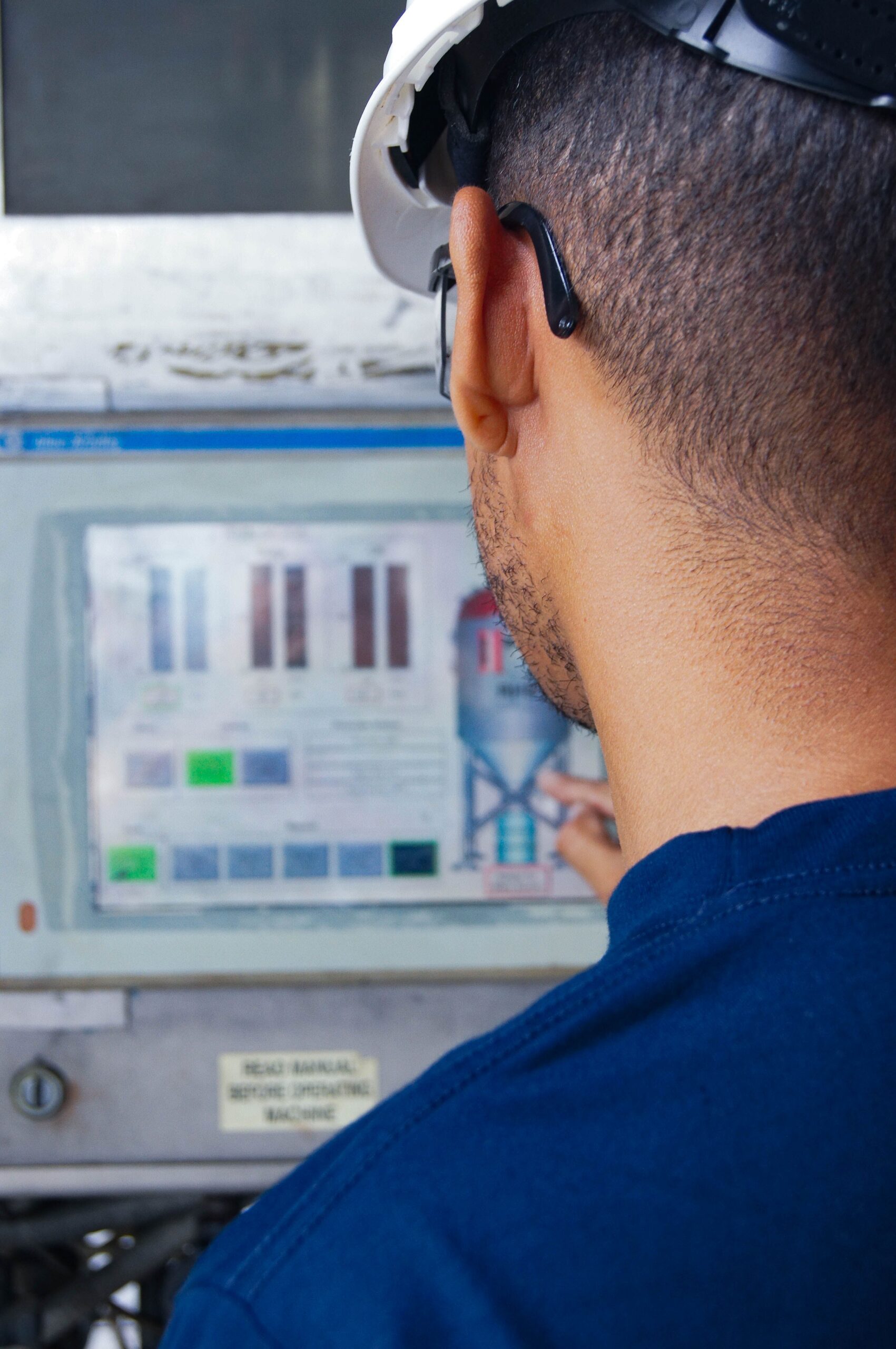 Engineer with hard hat working at an industrial control panel, displaying graphs.